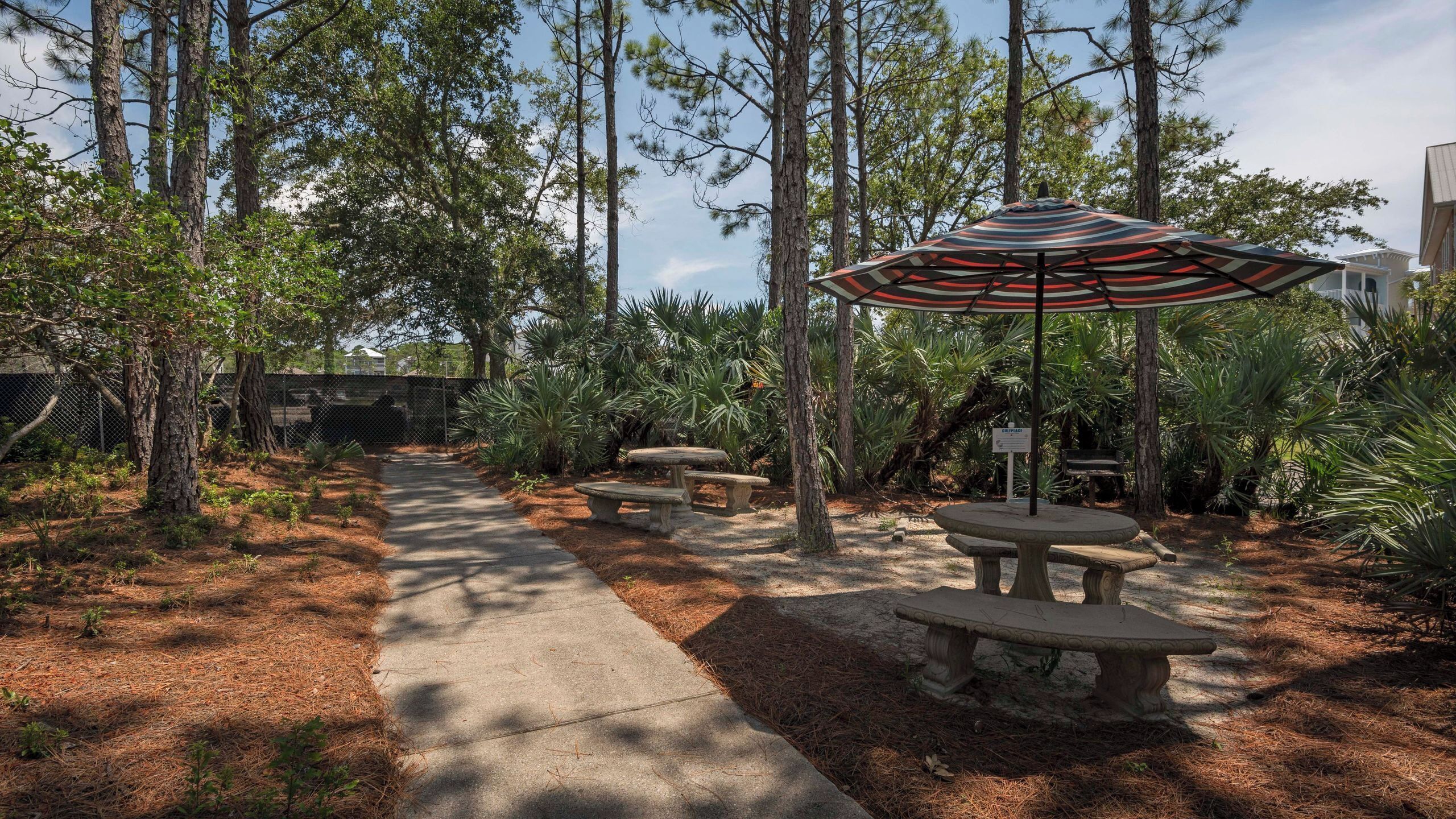 A pathway lined with benches and an umbrella, surrounded by trees and plants.