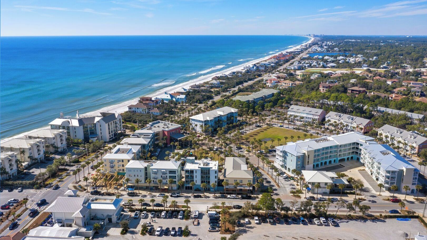 An aerial view of a coastal town with beachfront properties, a marina, and a mix of residential and commercial buildings.