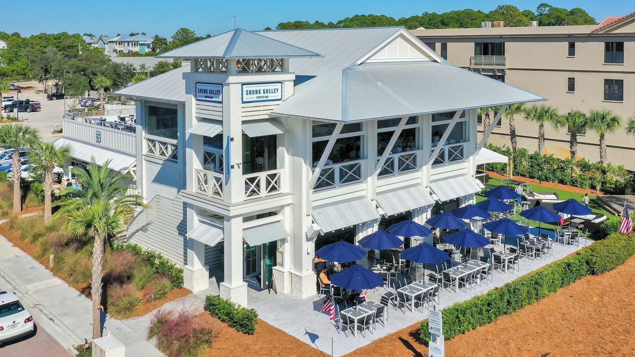 A coastal building with a bar named 'Shunk Gulley' and outdoor seating with umbrellas.