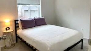 Un dormitorio con una cama, una ventana y una mesita de noche con una lámpara.
