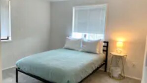 Un dormitorio con una cama, una mesita de noche y una ventana.