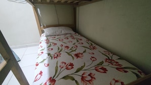 Ein kleines Zimmer mit einem Einzelbett, einer blumigen Bettdecke, einem Holzkopfende und einem Fenster mit Blick nach draußen.