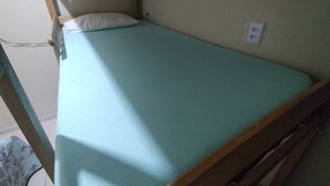 Ein Einzelbett mit Holzrahmen und einer hellblauen Matratze in einem Zimmer mit Fliesenboden.