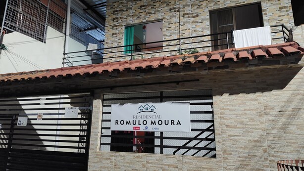 Ein Wohngebäude namens 'Romulo Moura' mit einer steinernen Fassade, einem Balkon mit rotem Dach und einem verschlossenen Eingang.