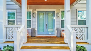 A porch with a wooden deck, white railings, and a blue door. - Amour La Mer by Avantstay Rooftop Patio, Pool Access, Walk to Beach (Panama City Beach)