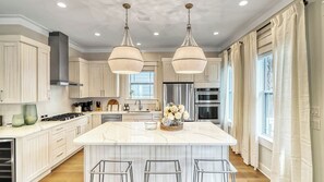 Un'ampia cucina con un'isola grande, elettrodomestici in acciaio inossidabile e illuminazione a sospensione.