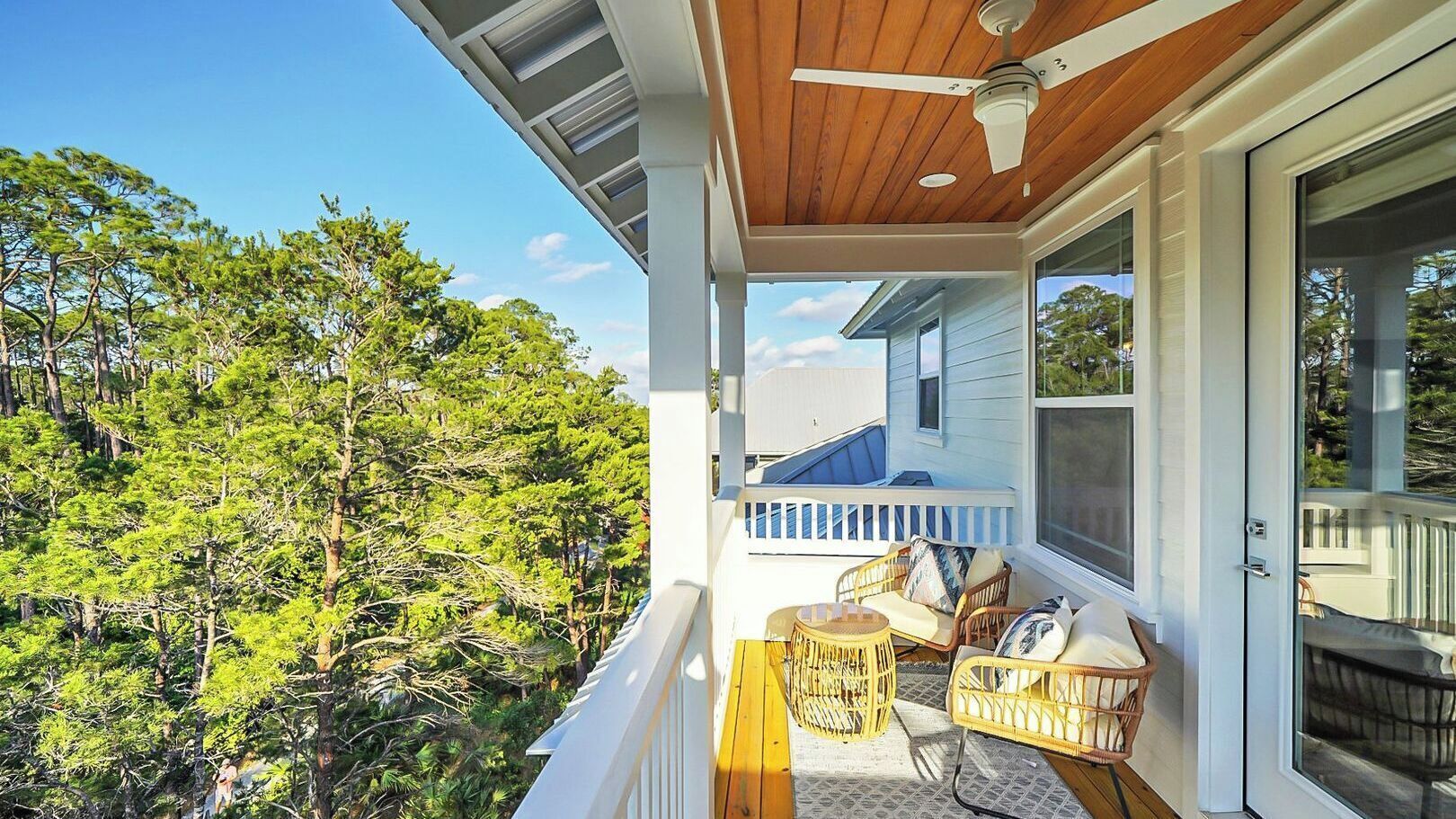 Une véranda aménagée avec des meubles d’extérieur, un ventilateur de plafond et une vue sur les arbres.