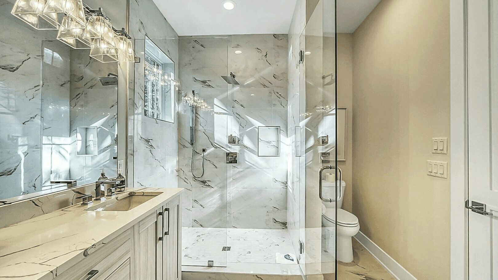 A modern bathroom with a glass-enclosed shower, a marble vanity, and a large mirror.