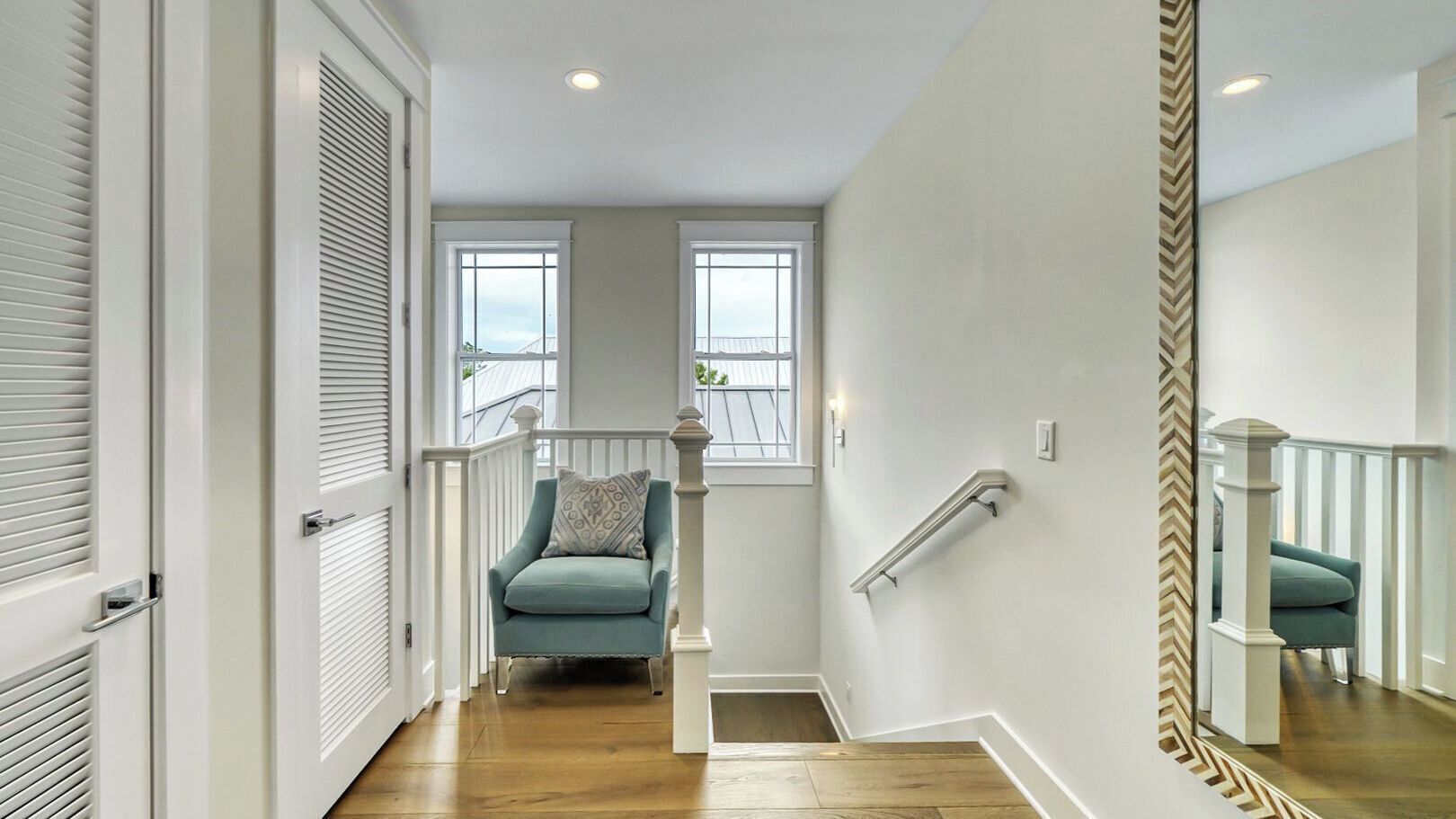 A staircase with a handrail, a teal chair, and a white railing.