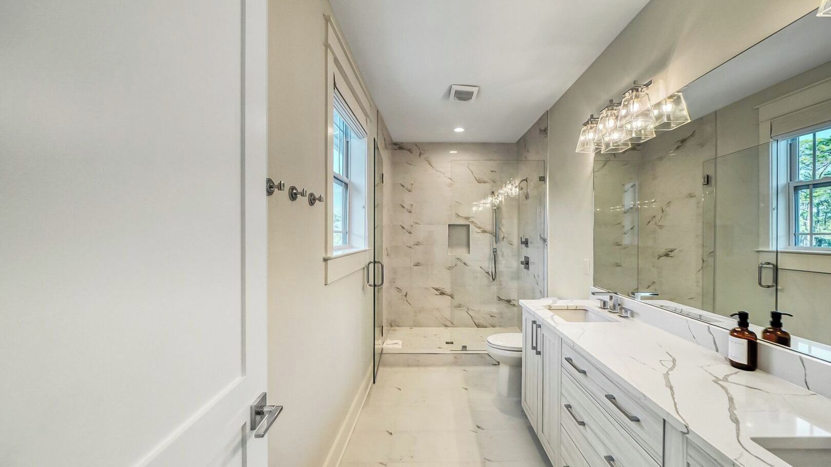 Un baño moderno con cabina de ducha de vidrio, un espejo grande y suelo de mármol.