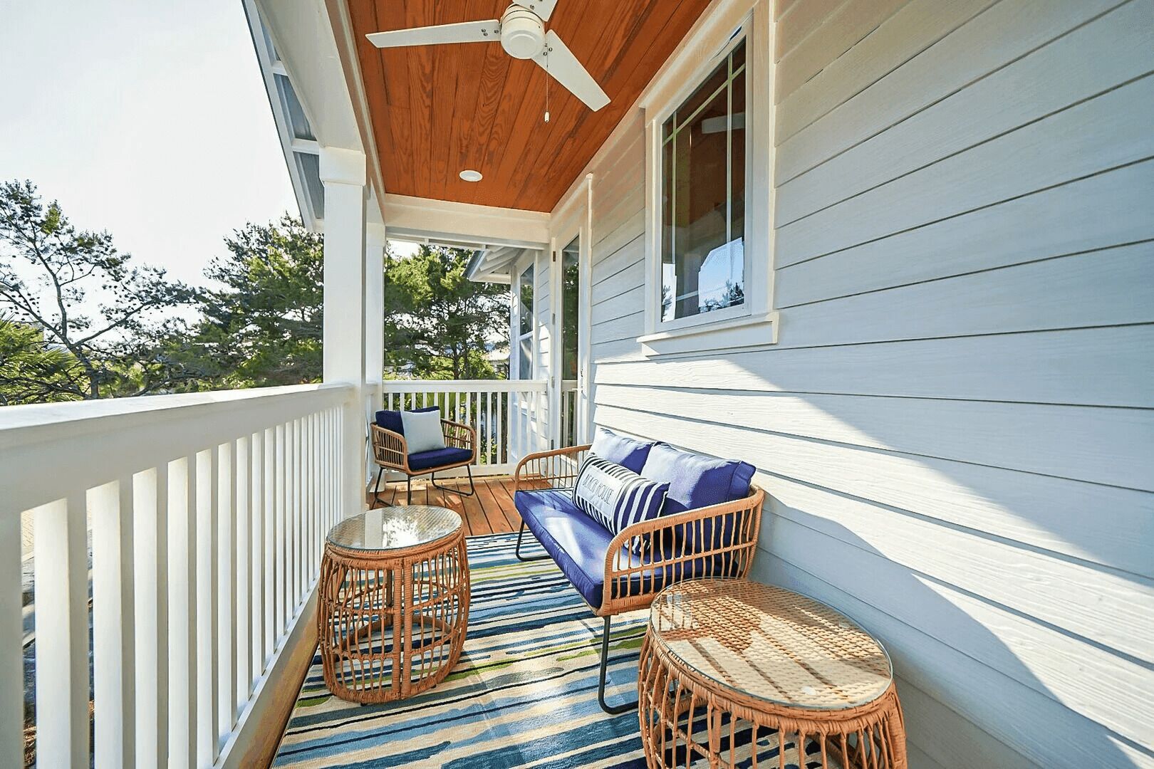 A covered porch with wicker furniture, a ceiling fan, and a view of trees.