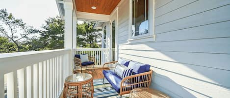 A covered porch with wicker furniture, a ceiling fan, and a view of trees.