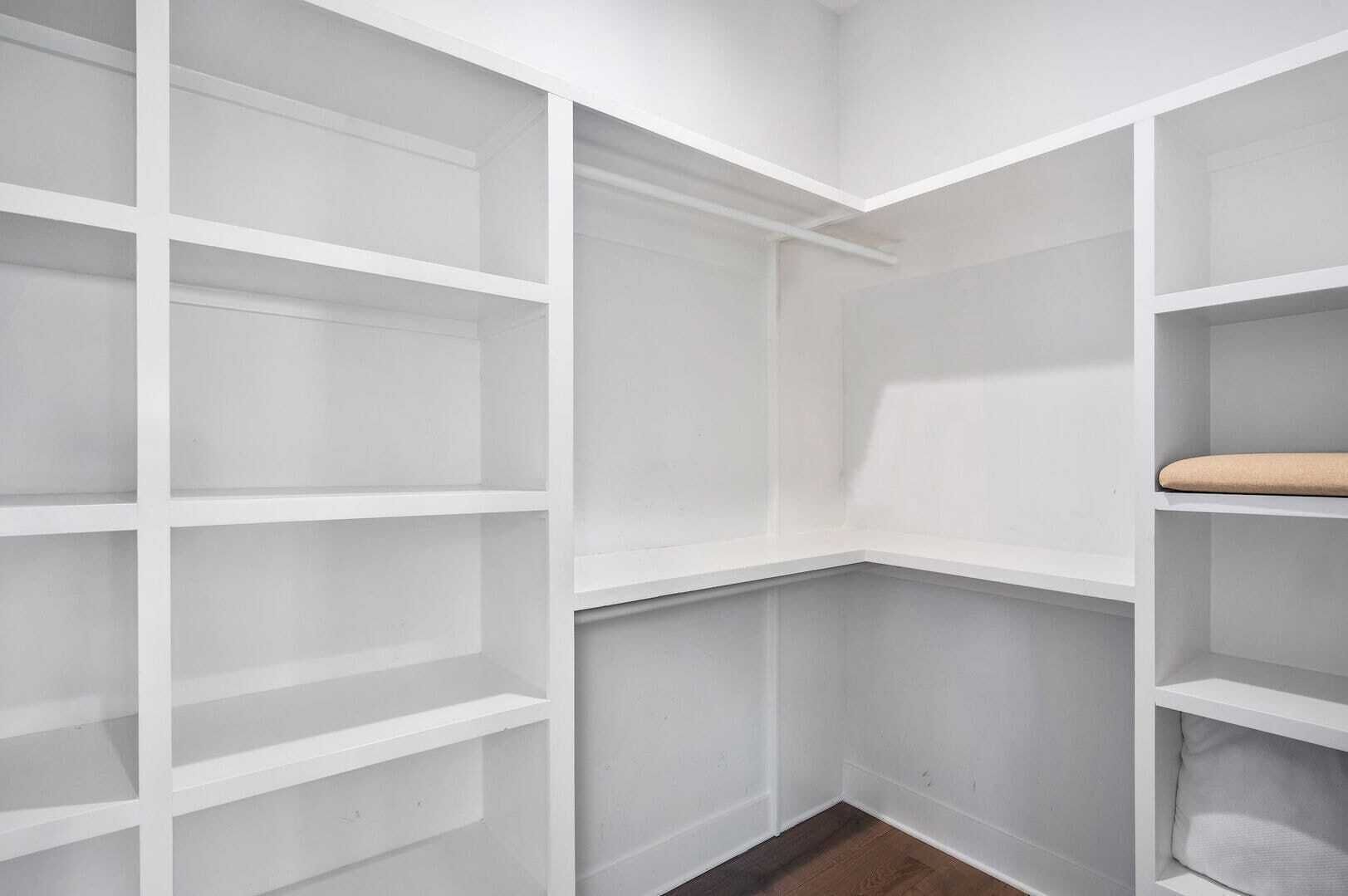 Una esquina de una habitación con estanterías blancas, algunas con cojines.