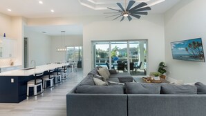 Ein geräumiger Wohnbereich mit grauem Sofa, eine Essecke mit langem Tisch und Stühlen sowie eine Küche mit weißer Arbeitsplatte.
