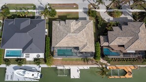 Vista aérea de una zona residencial con tres casas, cada una con piscina y muelle para embarcaciones.