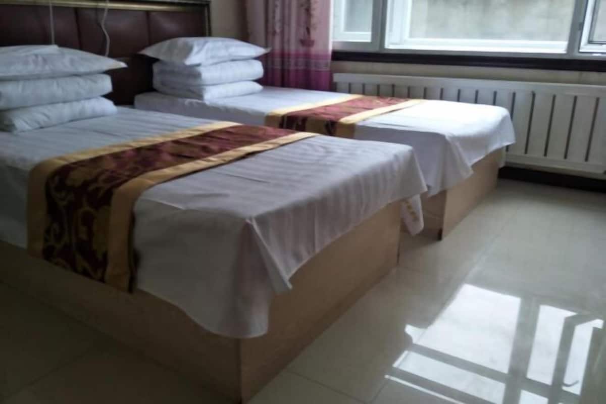 A room with two beds, a radiator, and a window.