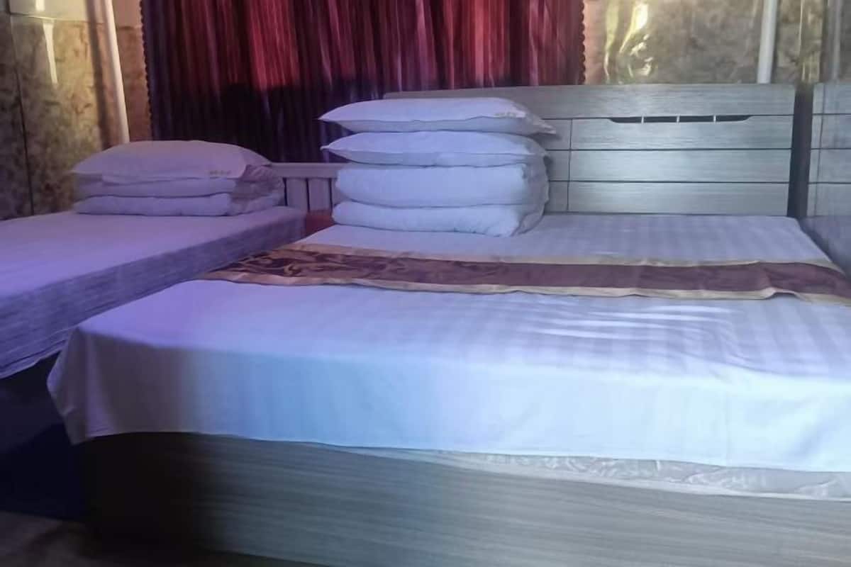 A bed with white bedding and a headboard, a bedside table, and a window with red curtains.