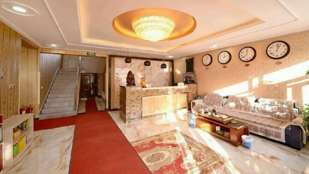Um hall de hotel com uma mesa de recepção, um sofá, uma escada e um candelabro.
