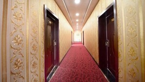 Um corredor de hotel com papel de parede estampado, carpete vermelho e portas duplas.