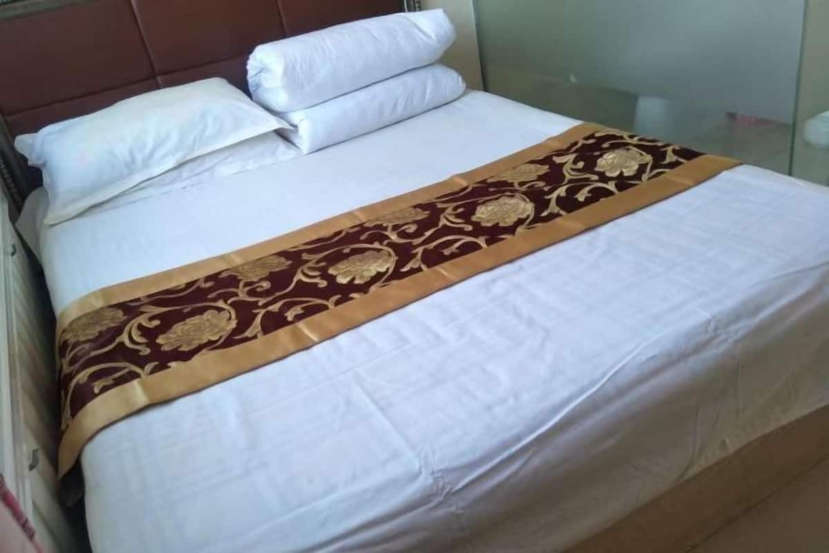 A bed with white linens, a brown and gold decorative bedspread, and a headboard.