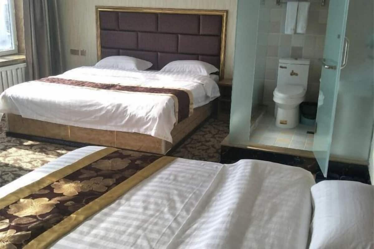 A hotel room with a large bed, a separate sofa, a bathroom with a glass enclosure, and a patterned carpet.