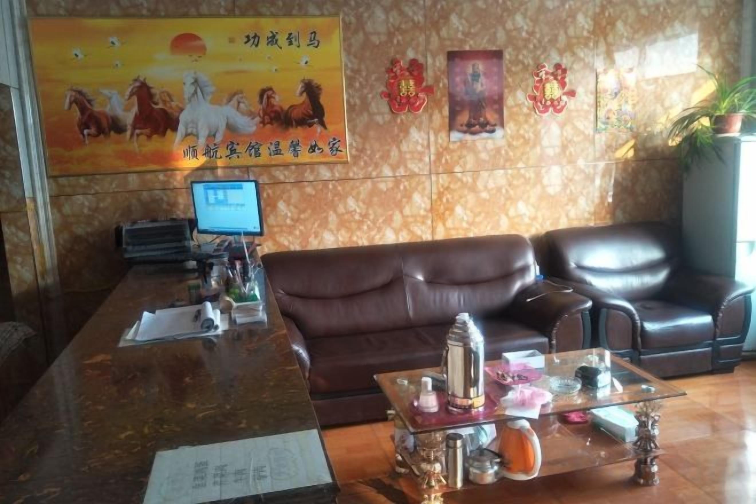 A reception area with a brown leather sofa, a glass coffee table with decorative items, a computer monitor, and a poster on the wall.