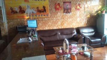 A reception area with a brown leather sofa, a glass coffee table with decorative items, a computer monitor, and a poster on the wall.