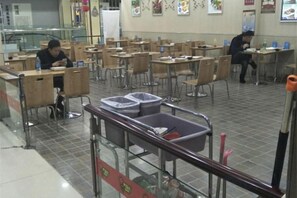 A cafeteria with multiple tables and chairs, a trash bin, and a person sitting at a table. - Shunhang Hotel (Harbin Taiping International Airport Branch) (Harbin)