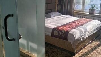 A bedroom with a bed, a window with a plant, and a radiator.