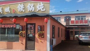 Restaurante com fachada vermelha e amarela, mesas ao ar livre e um carro estacionado na frente.