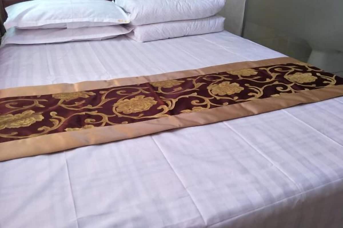A neatly made bed with a white duvet and a decorative gold and red runner.
