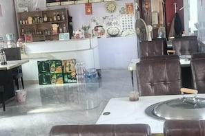 Interior de un restaurante con mesas, sillas, una barra con botellas y una pared decorada.