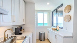A modern kitchen with white cabinets, a stainless steel sink, and a view of the ocean through a large window.