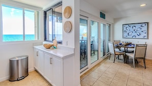 A modern kitchen with white cabinets, a stainless steel trash can, and a view of the ocean through large windows.