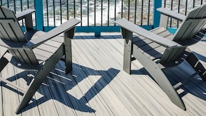 A wooden deck with two Adirondack chairs facing a calm sea and a distant island.