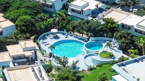 An aerial view of a resort with multiple swimming pools, lush greenery, and beachfront properties.