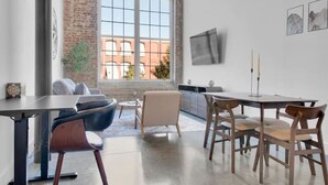 A modern interior with a dining area, a large window, and a brick wall. - Modern Escape | Pool | Easy Access to DT & More! (Greenville)
