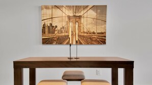 Una mesa de comedor con dos sillas acolchadas y una obra de arte enmarcada que muestra un puente y el horizonte de la ciudad.