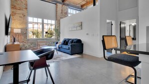 Una habitación amplia con un ventanal grande, un sofá azul, una mesa de comedor con sillas y una zona de cocina moderna.