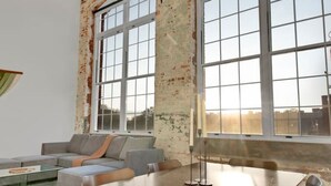 A spacious room with a large dining table, multiple chairs, a ceiling fan, and large windows offering a view of the city.