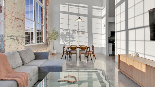A spacious living area with a large window, a dining table, and a modern sofa.
