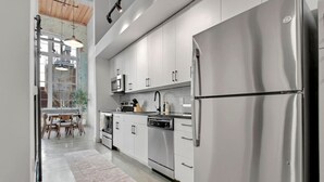 A modern kitchen with stainless steel appliances, white cabinetry, and a dining area with a wooden table and chairs.