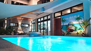 Ein Poolbereich mit tropischem Wandbild, Liegestühlen und einem großen Fenster mit Blick auf den Pool.