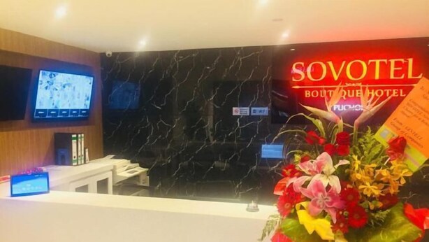 A hotel reception area with a black marble wall, a TV mounted on the wall, a reception desk, and a bouquet of flowers. - Sovotel Boutique Hotel @ Puchong (Puchong)