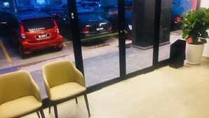 A hotel lobby with two yellow chairs, a potted plant, and a view of parked cars through large glass doors. - Sovotel Boutique Hotel @ Puchong (Puchong)