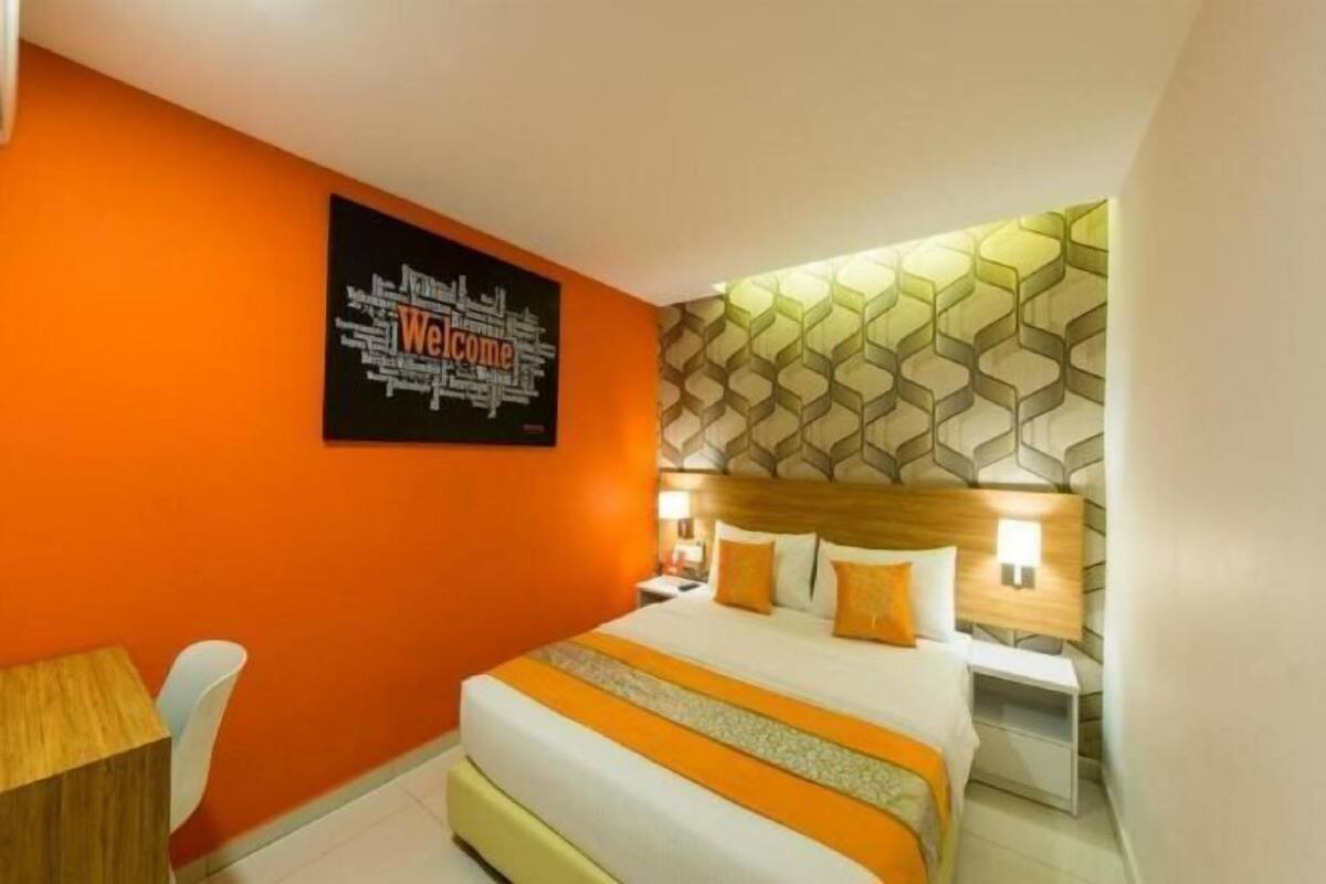 A hotel room with a bed, a desk, and a wall with a geometric pattern.