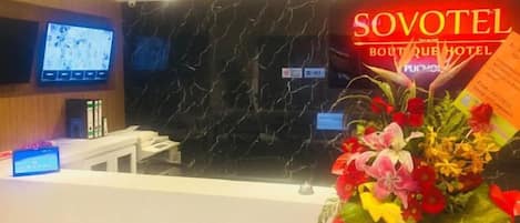 A reception desk with a television screen, a floral arrangement, and a sign for the SOVOTEL Boutique Hotel.