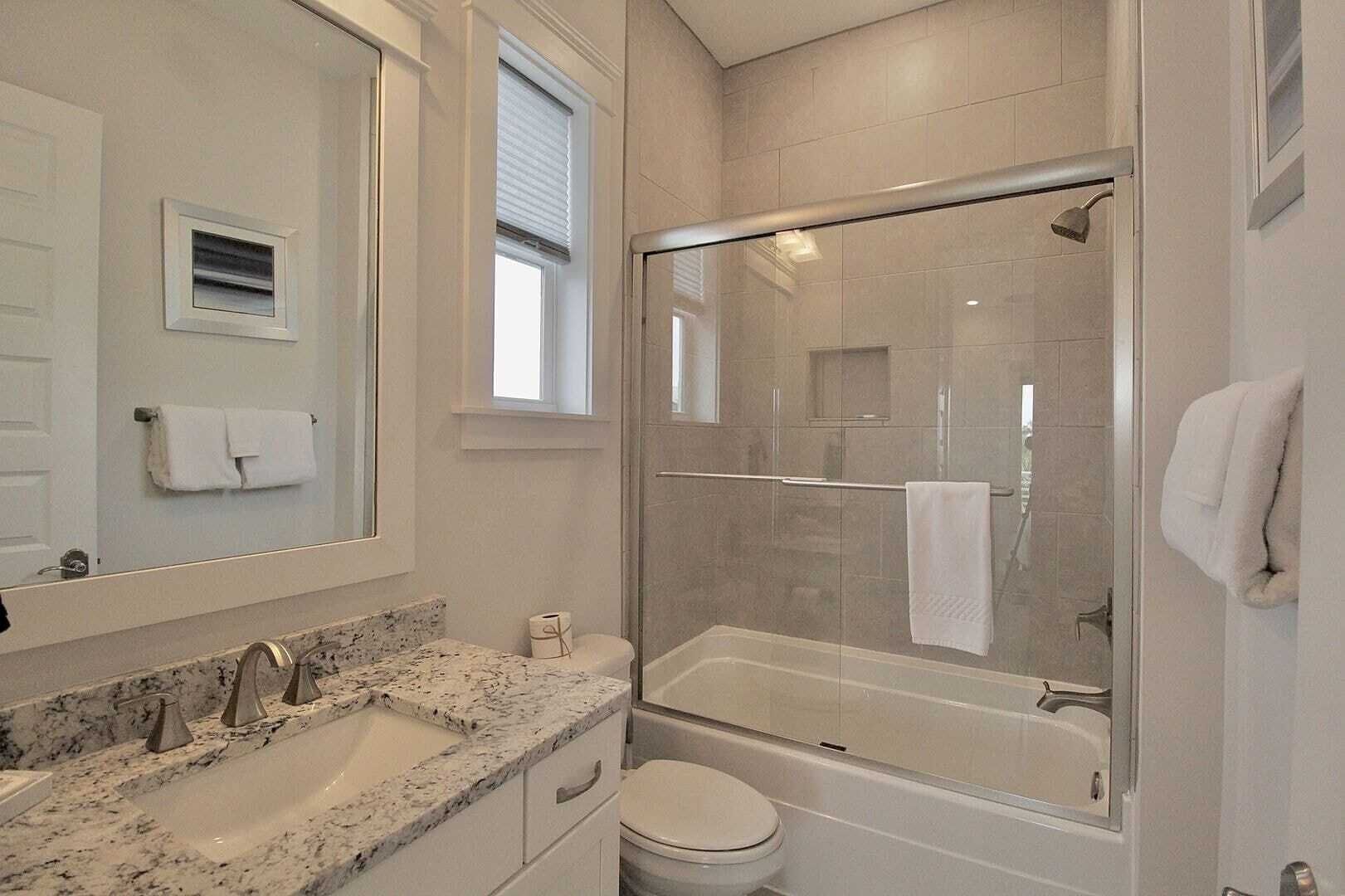 A modern bathroom with a glass-enclosed shower, a marble sink, and a toilet.