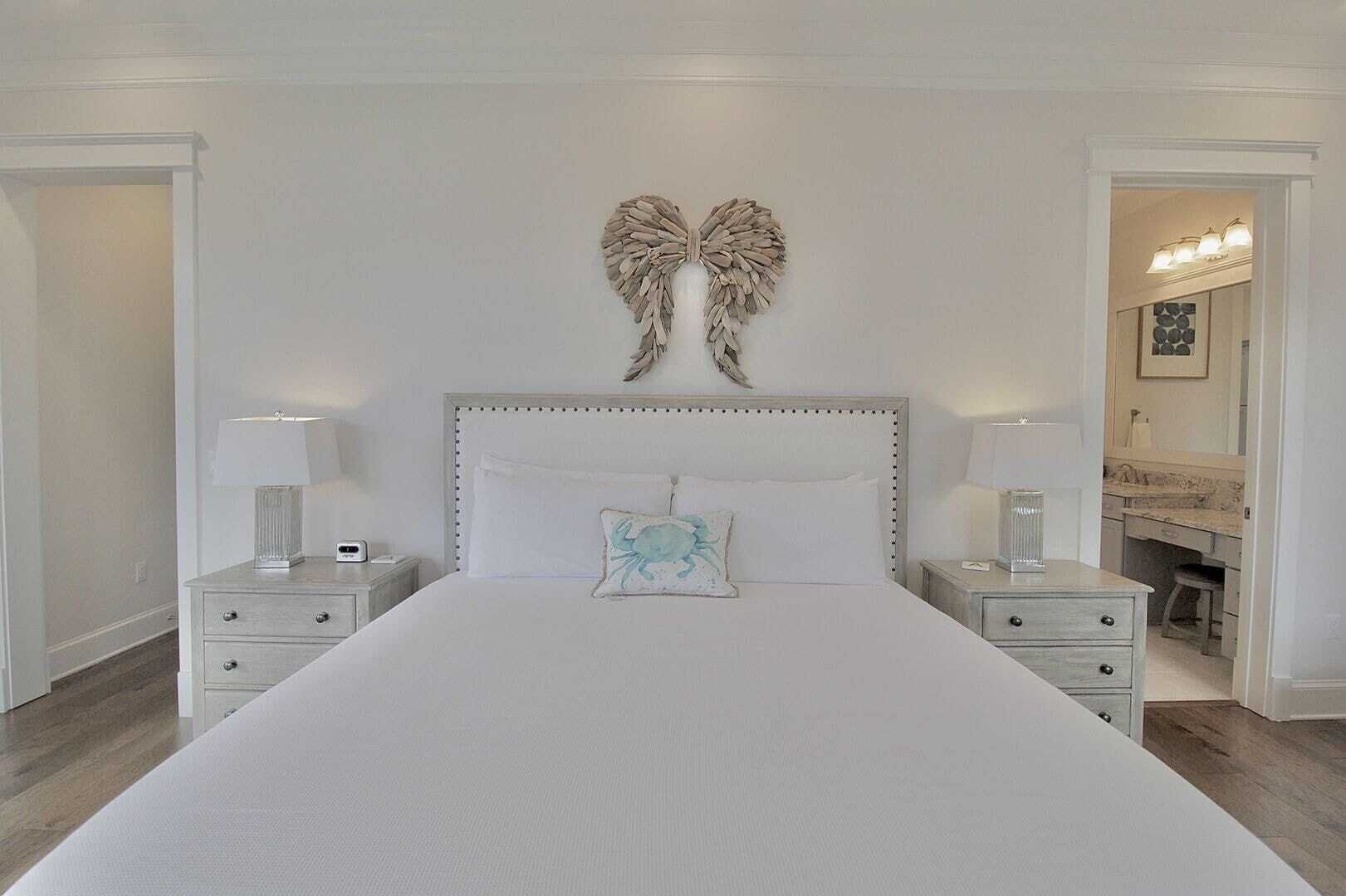 A bedroom with a large bed, two bedside tables, a wall-mounted decorative item, and a bathroom visible through an open door.