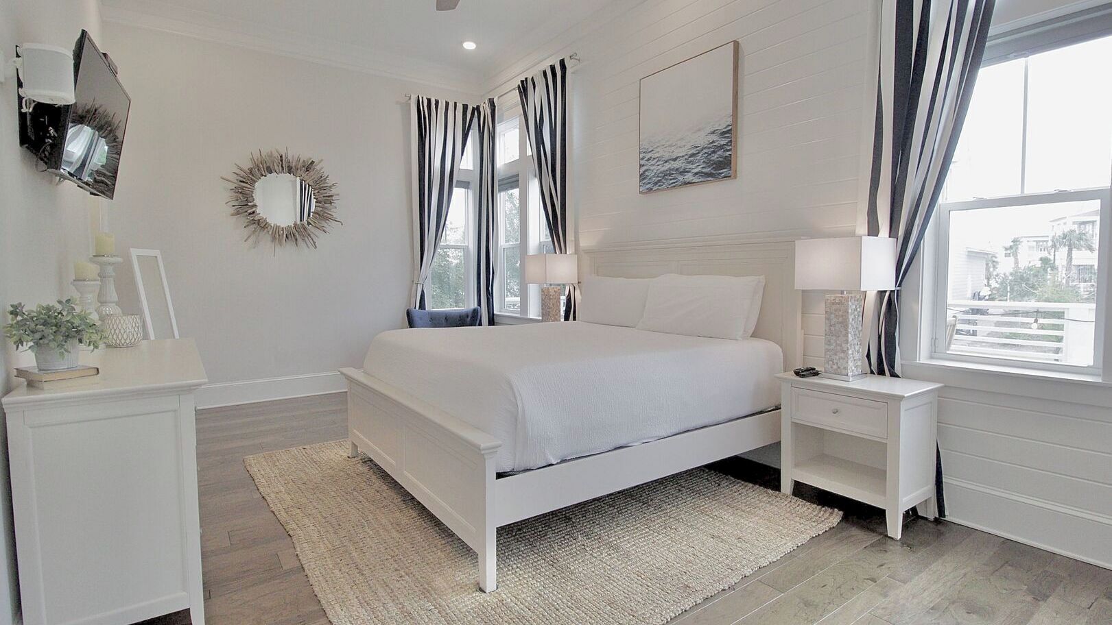 A bedroom with a bed, nightstands, a mirror, and a window with curtains.
